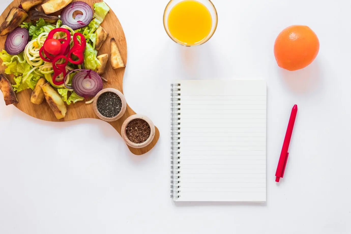 Gesunder Gemüsesalat; Saft; Obst; leerer Notizblock und Stift vor weißem Hintergrund.